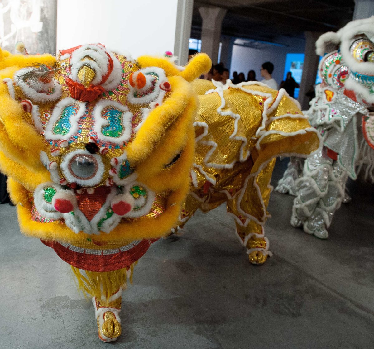 Chinese lion dancers in costumes, one showing a yellow lion and the other showing a white lion